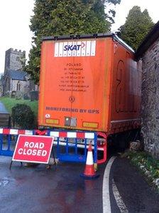 Lorry wedged between churchyard and house in Brompton Regis