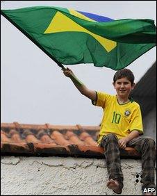 A boy waves a Brazilian flag as he sits on a roof to watch Brazil's national football team train on 23 May