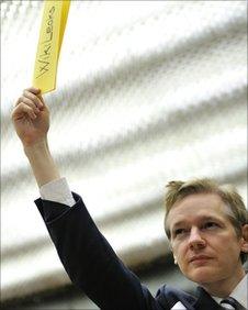 Julian Assange holds a piece of paper, saying Wikileaks