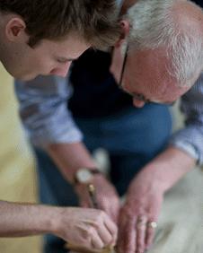 A man teaching a younger man how to cut glass