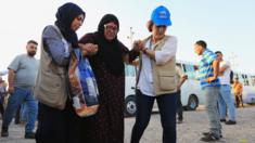 UN aid workers help a displaced Syrian woman who fled the Turkish offensive in northern Syria, at a refugee camp in Dohuk, Iraq