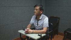 El escritor chino Liu Yongbiao bajo custodia policial sentado en una silla y con los brazos sobre una mesa