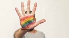 A man holding up a hand with a LGBT rainbow flow painted on his palm