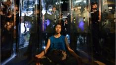 A woman (C) meditates in front of a line of riot police standing guard with their shields outside the government headquarters in Hong Kong early on June 12, 2019