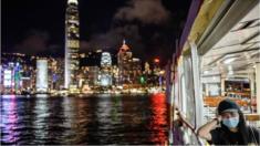 A woman wearing a face mask takes a Star Ferry in Victoria Harbour from Kowloon side to Hong Kong Island (back) on July 27, 2020