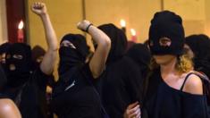 Women covering their faces with black scarves demonstrate, carrying torches