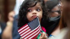 A child holds the US flag as the Citizenship and Immigration Services welcomes 200 new citizens from 50 countries during a ceremony in New York, 3 July 2018