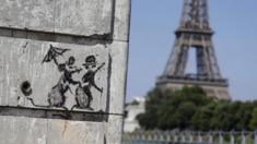 A recent artwork by street artist Banksy is pictured in Paris on 27 June 2018, near the Eiffel Tower (R)