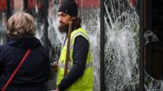 A man takes part in the Paris clean-up after the 8 December protest, against a backdrop of smashed windows