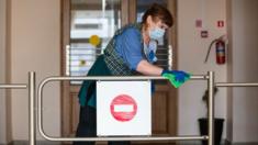 A cleaner sanitises a railing inside a school building