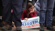 Young girl sits with Elizabeth Warren campaign sign at a New Hampshire rally, February 2020