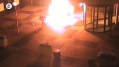 A hooded figure runs away from an explosion of flame near the office door