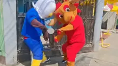 Two World Cup mascots breaking into an iron gate with a metal pole.