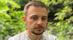 Christopher Banks is standing alongside the River Tonge in Bolton. It is a bright dry day and he is wearing a grey t-shirt. Green foliage and the water can be seen in the background.