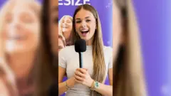 A young woman with long hair stands holding a microphone