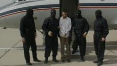 This frame grab released February 23, 2010 from Iranian state TV shows Sunni Muslim rebel leader Abdolmalek Rigi under armed guard following his arrest. Man is in handcuffs surrounded by four masked men, in front of a small plane