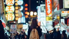 Un chica camina con una mochila por mitad de una calle de Tokio, iluminada por anuncios de neón y otros más tradicionales.