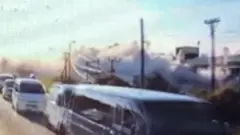 A queue of cars can be seen with a big cloud of grey smoke visible behind the powerlines.
