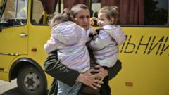 A father holds his young twin daughters as they wait to be evacuated from Lysychansk, eastern Ukraine. Photo: May 2022