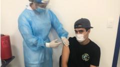 Abdel está sentado enquanto enfermeira aplica a vacina contra a covid-19