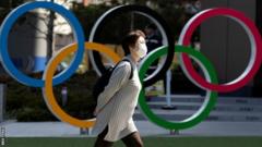 A woman wearing a protective mask walking in front of Olympic rings at the Olympics Museum in Tokyo