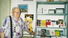 Siegfried Ellwanger, um idoso branco, calvo, de óculos, ao lado de sua coleção de livros