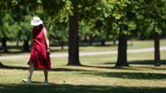 A woman in a red dress and sun hat walks by some trees