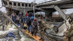 People cross the river via a makeshift bridge as they flee the frontline town of Irpin, near Kyiv, Ukraine - 7 March 2022.
