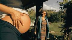 Marilanda standing next to a pregnant woman's baby bump on the left hand side