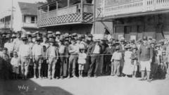 Retrato de quarentena na Chinatown de Honolulu, em 1899, em foto preto e branco; nela, se vê muitas crianças e adultos atrás de cordas, com guarda em vão protegido por corda de controle