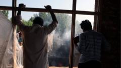 Kashmiris watch as people try to douse the fire at a damaged residential house where two alleged militants were killed in a military operation in Srinagar, Indian Administered Kashmir on 16 July 2021.