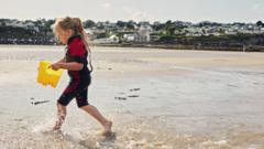 Little girl in a wetsuit on the beach with a bucket full of water from the sea