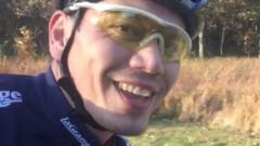 Tom Justice smiling to camera while wearing a cycle helmet and cycling shirt in front of trees