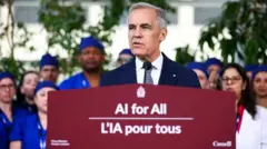 Canada's Prime Minister Mark Carney announces a new federal AI agenda, at Toronto General Hospital. He is standing in front of several healthcare workers who are wearing scrubs and lab coats. He stands behind a podium that says "AI for All - L'IA pour tous".