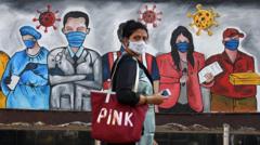 woman wearing a mask walks past a graffiti raising awareness about wearing of facemasks to avoid the risk of the COVID-19 coronavirus in Mumbai