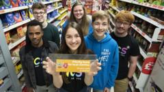 A group of teenagers holding a supermarket sign highlighting priority items for food banks.