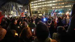James Manning/PA Wire A crowd gathered around during a vigil outside the Australian High Commission in central London. It's night time and a handful of UK and Israeli flags can be seen waved in the sky.