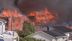 Several houses on fire engulfed in dark smoke, with untouched houses in front of them
