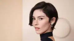 Gracie Abrams poses on the red carpet of the 2026 Oscars, in a black dress with a choker, and sparkling diamond earrings.
