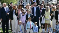 Getty Images Crowd of people, many children, dressed in beige and pastels, with Trump standing on one side in dark suit
