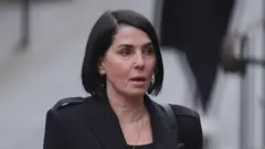 PA Media Sadie Frost, a woman with short, straight black hair, stares ahead with a blank expression. She is wearing a black jacket and gold necklace over a black top.