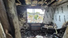The McConnell family in a burnt-out room. Everything is black and burnt.