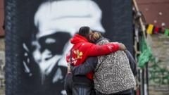 Duas pessoas de costas para a foto e abraçadas, em frente a grafite de George Floyd pintado