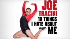 Joe in a leotard on a poster advertising his tour, called 10 things I hate about me. The leotard is black and has red sleeves. His legs are bare and he is wearing black lace-up dance shoes.
