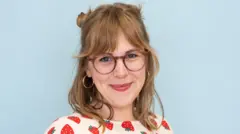 Jennie Lennick smiles at the camera. She is wearing glasses and a top with a strawberry pattern