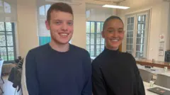 Students Alexandre Hubert and Valentine Guillot stand in class and smile at the camera