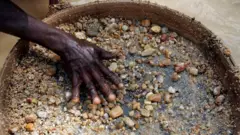 The hand of a diamond miner in Sierra Leone has he sieves gravel and smaller stones in the hope of finding the precious gems
