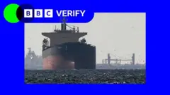 Cargo ships in the Gulf, near the Strait of Hormuz, as seen from northern Ras al-Khaimah. The ship in the foreground is a large tanker with a red hull and a white stern.  