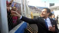 AFP Reelected President Juan Orlando Hernandez waves to the crowd at his arrival to the inauguration ceremony at the Tiburcio Carias Andino national stadium, in Tegucigalpa, on January 27,
