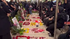 People sit in front of flowers commemorating people who have died